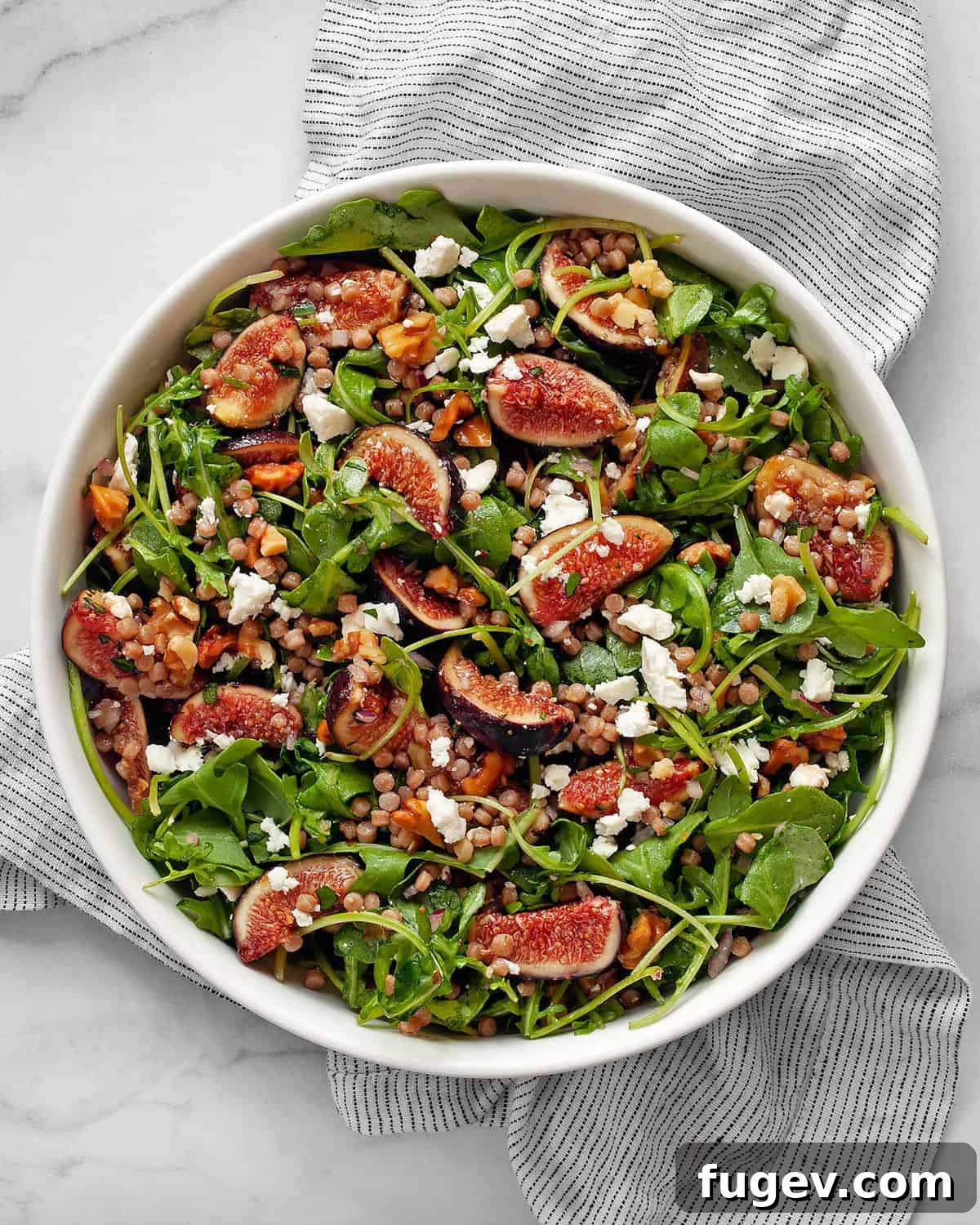 Mediterranean Fig, Chevre and Arugula Couscous Salad 2 A vibrant bowl of fresh fig salad featuring arugula, couscous, quartered figs, crumbled goat cheese, and toasted walnuts, drizzled with balsamic vinaigrette.