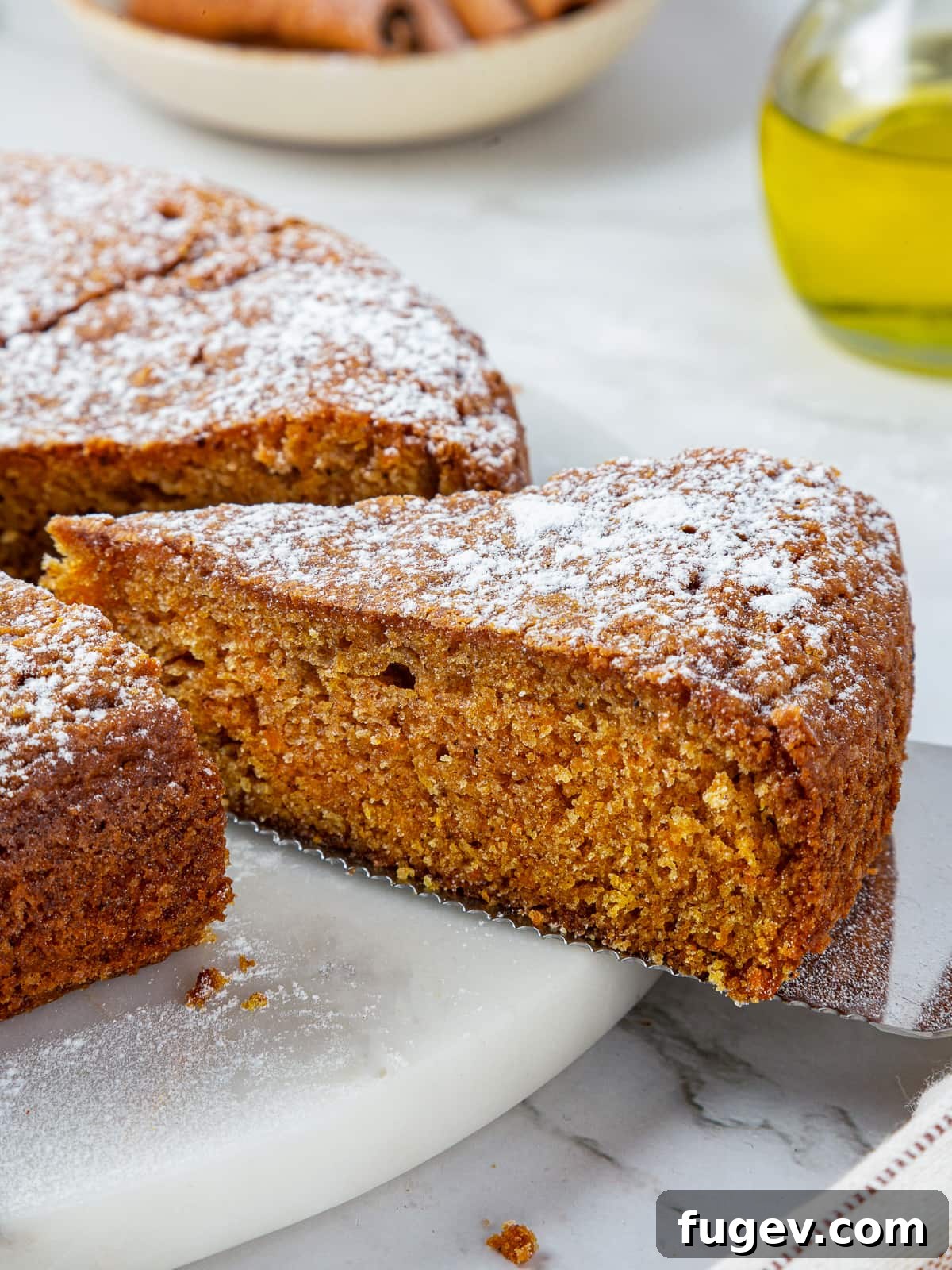 Velvety Pumpkin Olive Oil Cake 12 A magnificent full pumpkin olive oil cake, beautifully centered on a pristine white ceramic cake stand, expertly sliced and poised for sharing with guests.