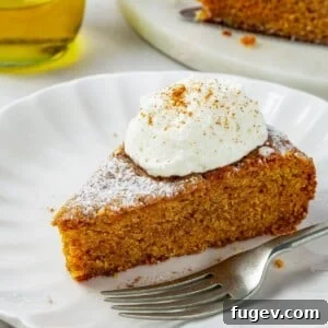 A silver fork positioned next to a beautifully soft pumpkin olive oil cake on a dessert plate, with delicate crumbs falling onto the table, inviting a taste.
