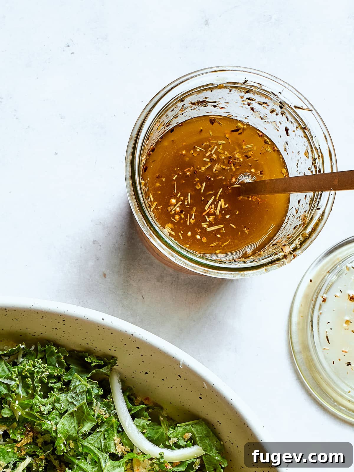 Effortless Homemade Italian Dressing 2 Homemade Italian salad dressing in a clear jar with flecks of oregano and cheese, ready to be served, accompanied by a golden spoon.