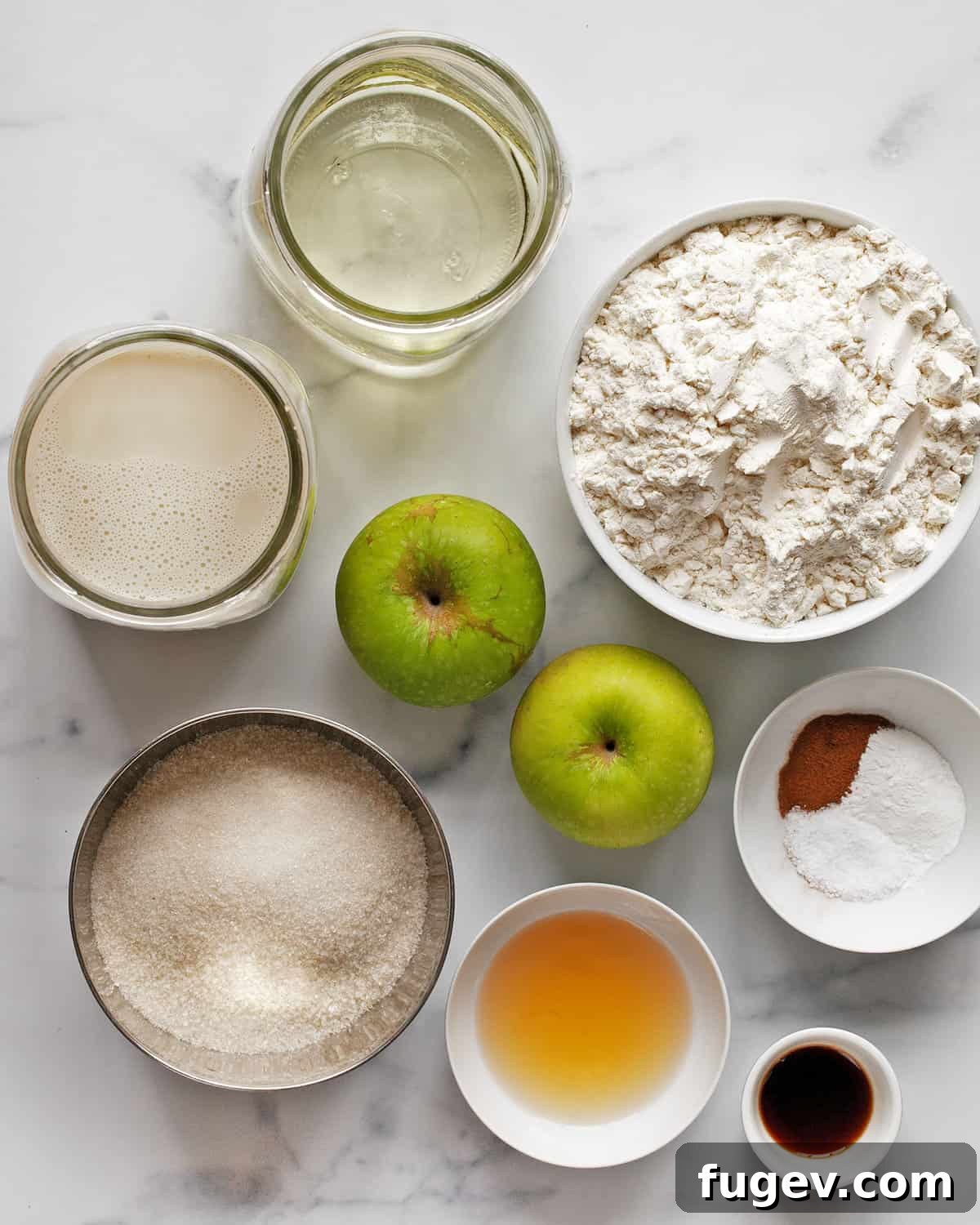 Spiced Apple Cinnamon Vegan Muffins 3 A flat lay of all the fresh ingredients needed for vegan apple cinnamon muffins: flour, cinnamon, apples, sugar, baking powder, salt, oil, plant-based milk, vinegar, and vanilla extract, ready for baking.