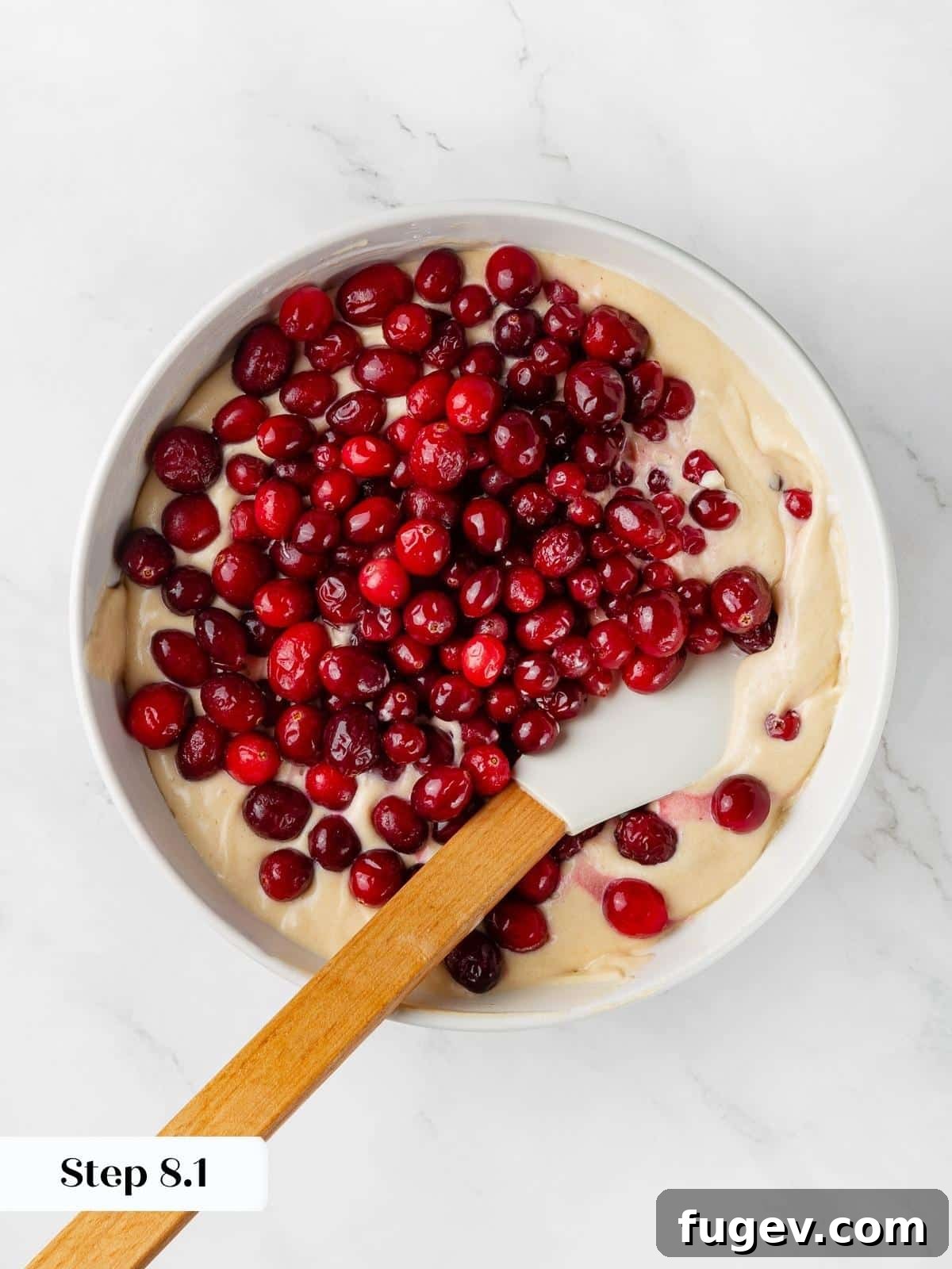 Ultimate Cranberry Cake 6 Fresh, vibrant cranberries being gently folded into thick, creamy cake batter using a spatula, ready for baking.