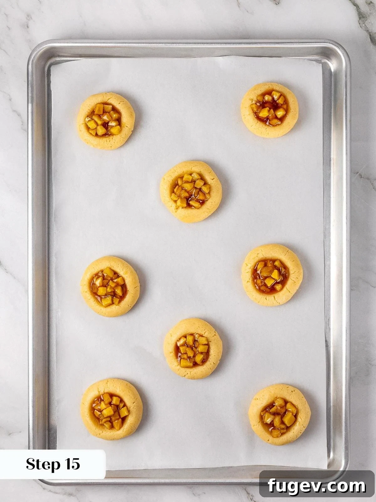 Warm Apple Spice Cookies 13 Unbaked cookie dough rounds on a baking tray, each generously filled with small spoonfuls of the homemade apple pie filling, neatly contained within the indentations.
