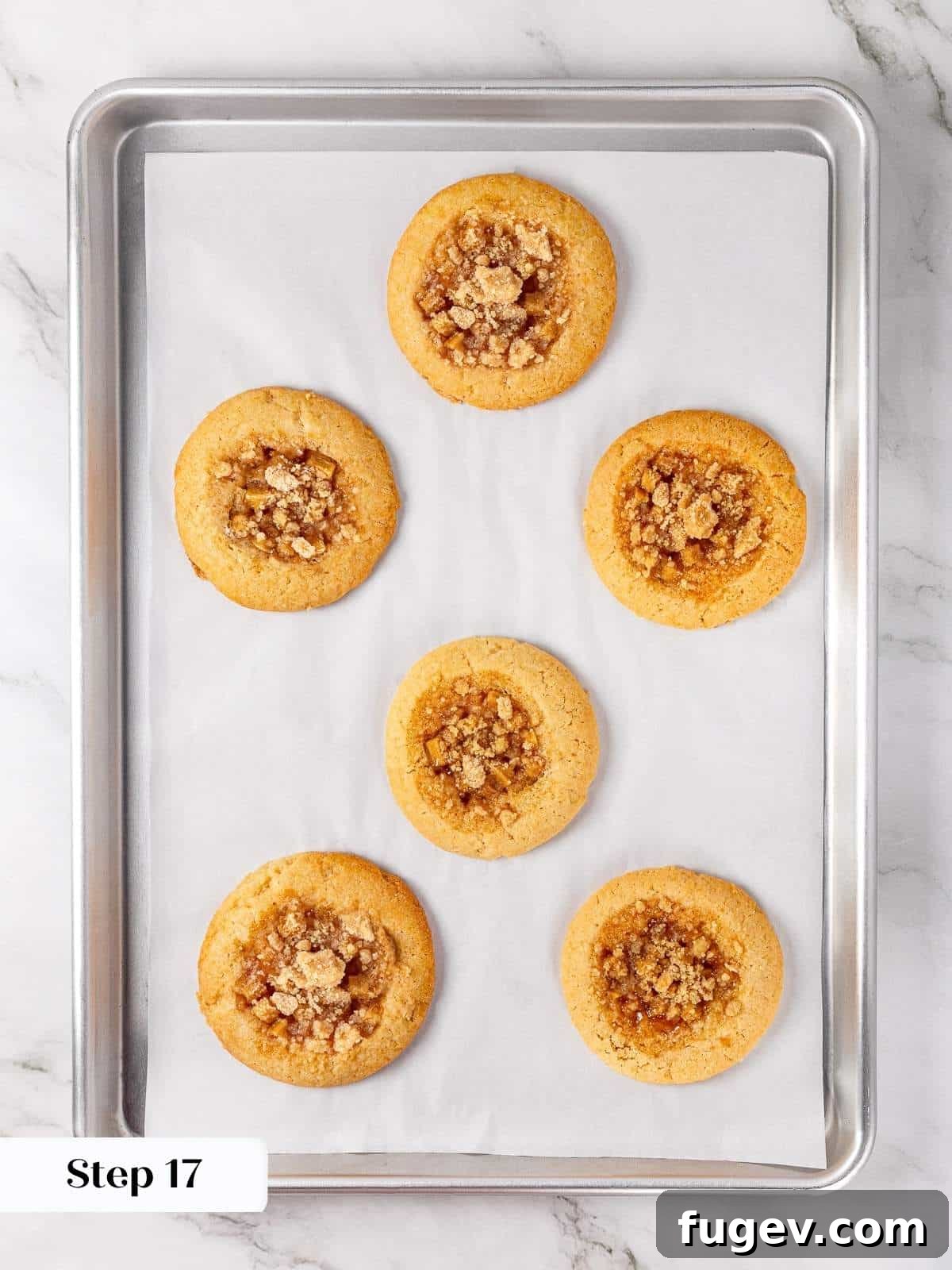 Warm Apple Spice Cookies 15 Freshly baked apple pie cookies cooling on a parchment-lined baking sheet after being removed from the oven, their edges golden brown and centers bubbling with apple goodness.