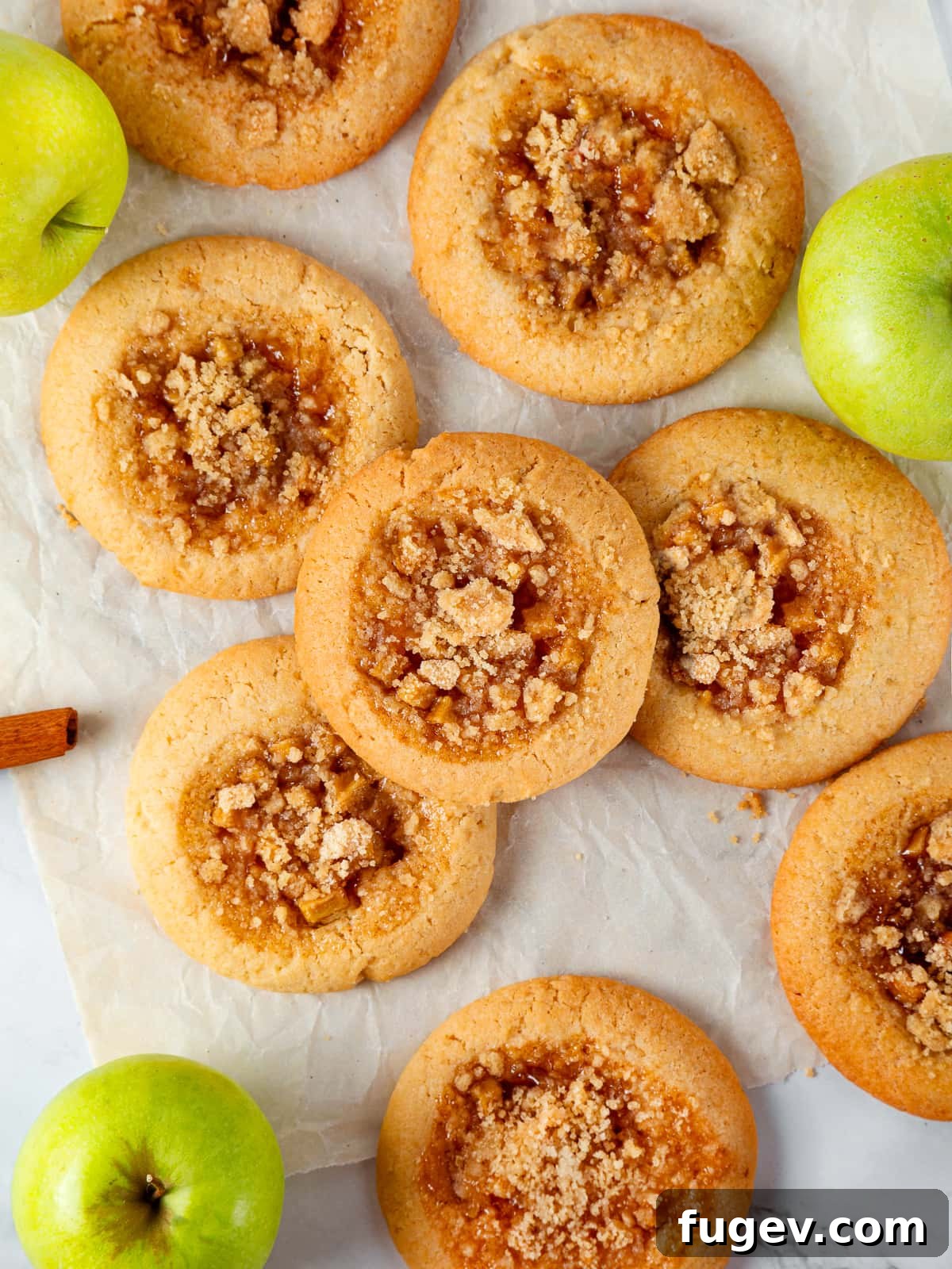 Warm Apple Spice Cookies 17 Assorted apple pie cookies spread on a rustic wooden table, showcasing their golden crumble tops, soft centers, and overall delicious appeal in a charming group setting.