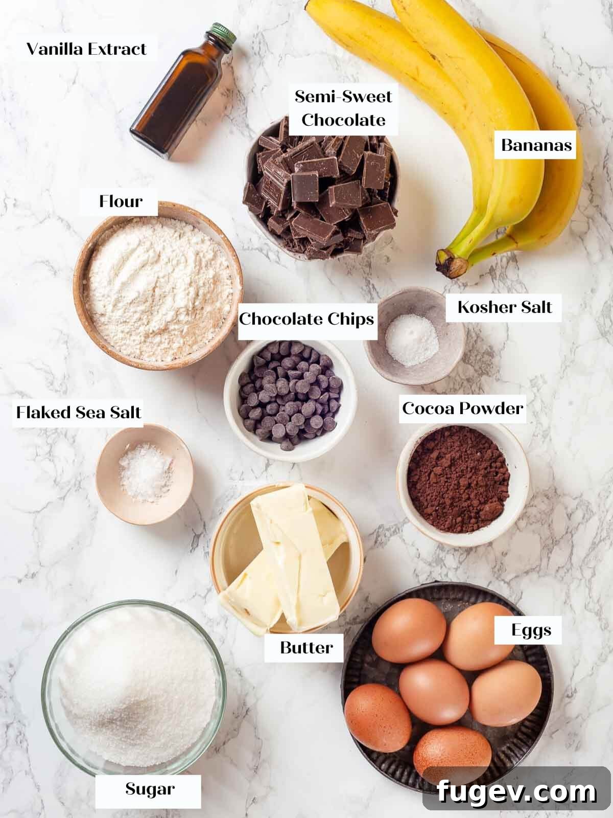 Fudgy Banana Brownies 4 All the necessary ingredients for baking banana brownies, neatly arranged on a white countertop, including chocolate, bananas, eggs, flour, and butter.