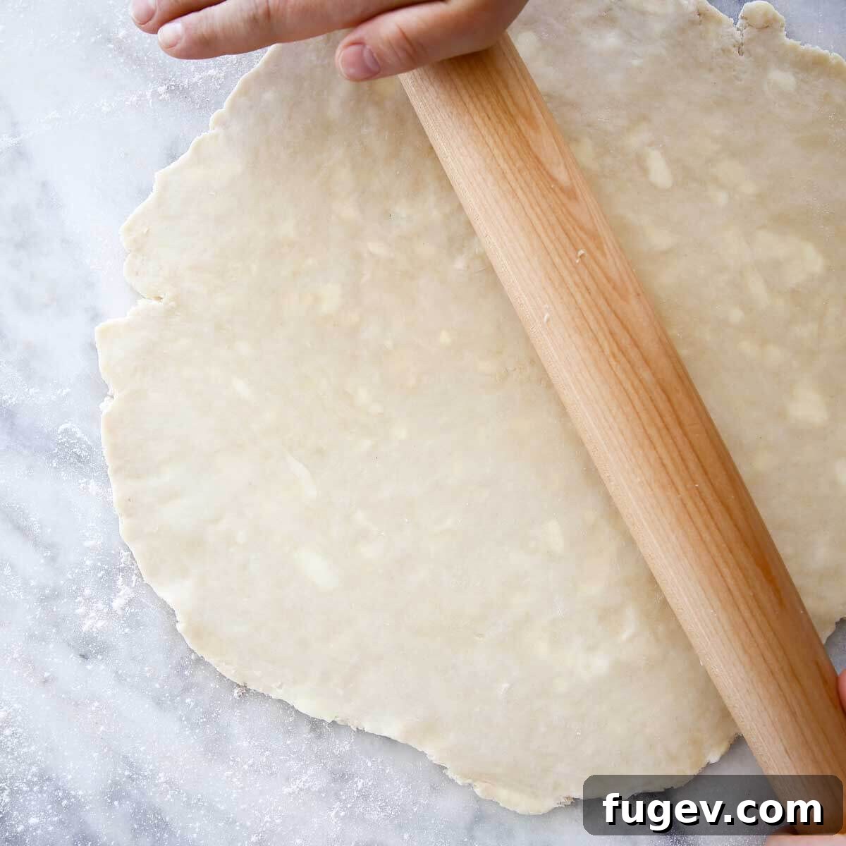 Rich Flaky Butter Pastry 4 Pie dough being rolled out thin on a floured marble surface with hands on rolling pin.