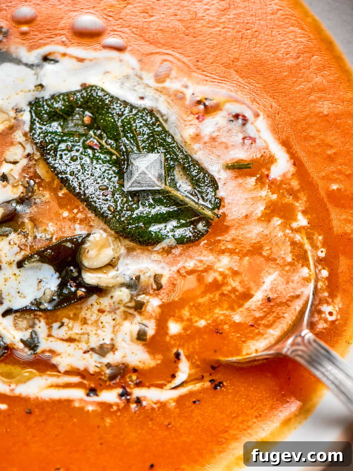 Creamy Vegan Pumpkin Harvest Soup 2 Spoon entering the bowl reveals the thick, comforting consistency of the warm pumpkin soup, garnished with a sprinkle of fresh herbs.
