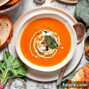 Bright orange vegan pumpkin soup served in a bowl with a spoon, fresh herbs, and small pieces of rustic bread on the side.