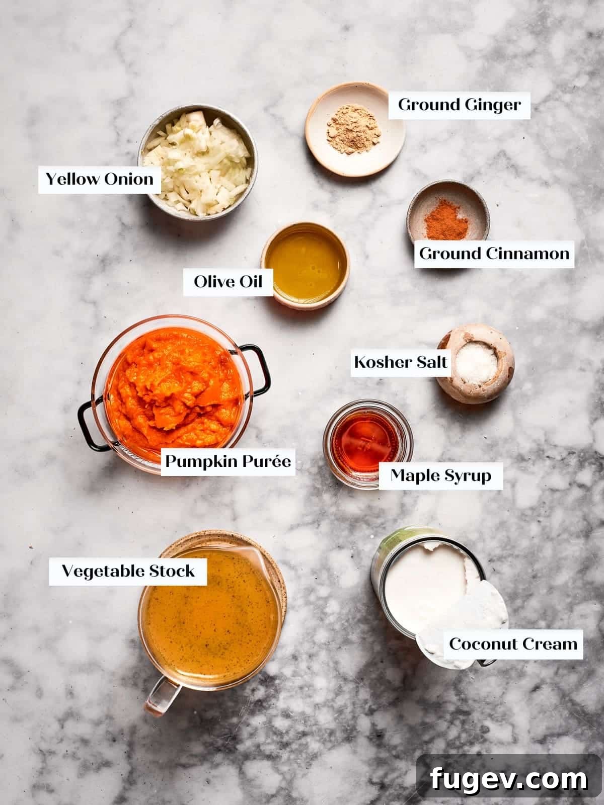 Creamy Vegan Pumpkin Harvest Soup 4 Key ingredients for vegan pumpkin soup artfully arranged on a countertop, including canned pumpkin puree, coconut cream, a yellow onion, fresh ginger, cinnamon, and vegetable stock.