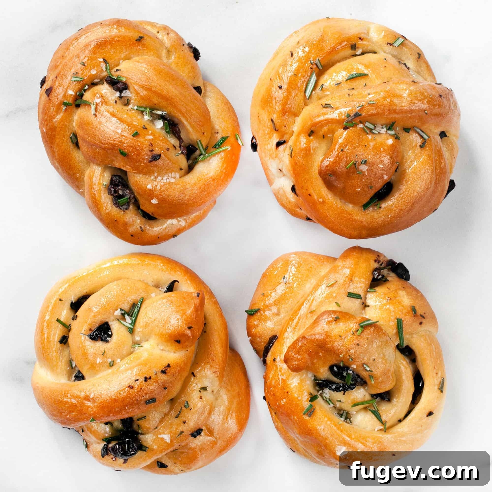 Savory Rosemary Olive Twists 2 Freshly baked Rosemary Olive Knots on a wire rack, garnished with fresh rosemary sprigs and whole Kalamata olives, emphasizing their homemade goodness.