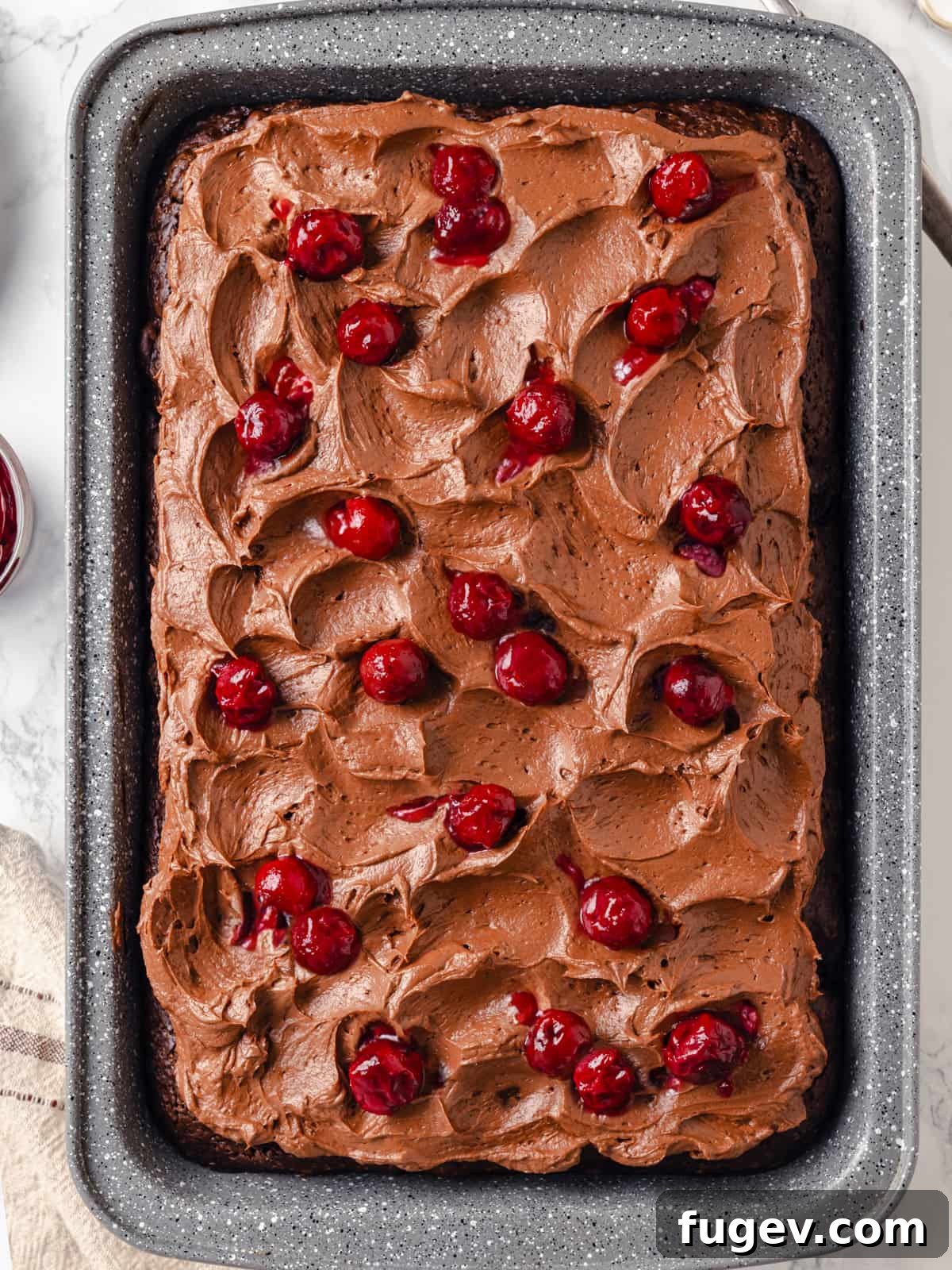 Decadent Chocolate Cream Cheese Dream 10 A rectangular chocolate cake, unfurled, beautifully topped with swirled chocolate cream cheese frosting and fresh cherries, ready to be sliced.
