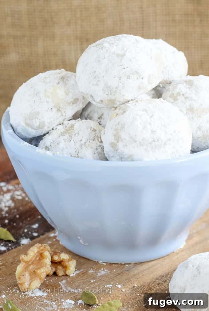 Fragrant Cardamom Walnut Snowdrifts 4 A trio of Cardamom Walnut Snowballs arranged on a wire rack, glistening with powdered sugar.