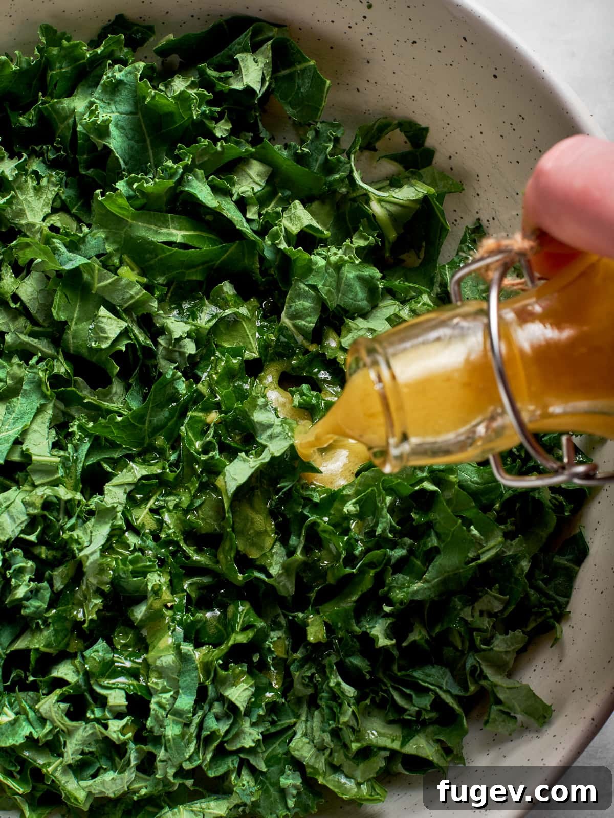 Sparkling Champagne Vinaigrette 9 Champagne vinaigrette poured generously over kale salad greens in a large serving bowl, ready to be tossed.