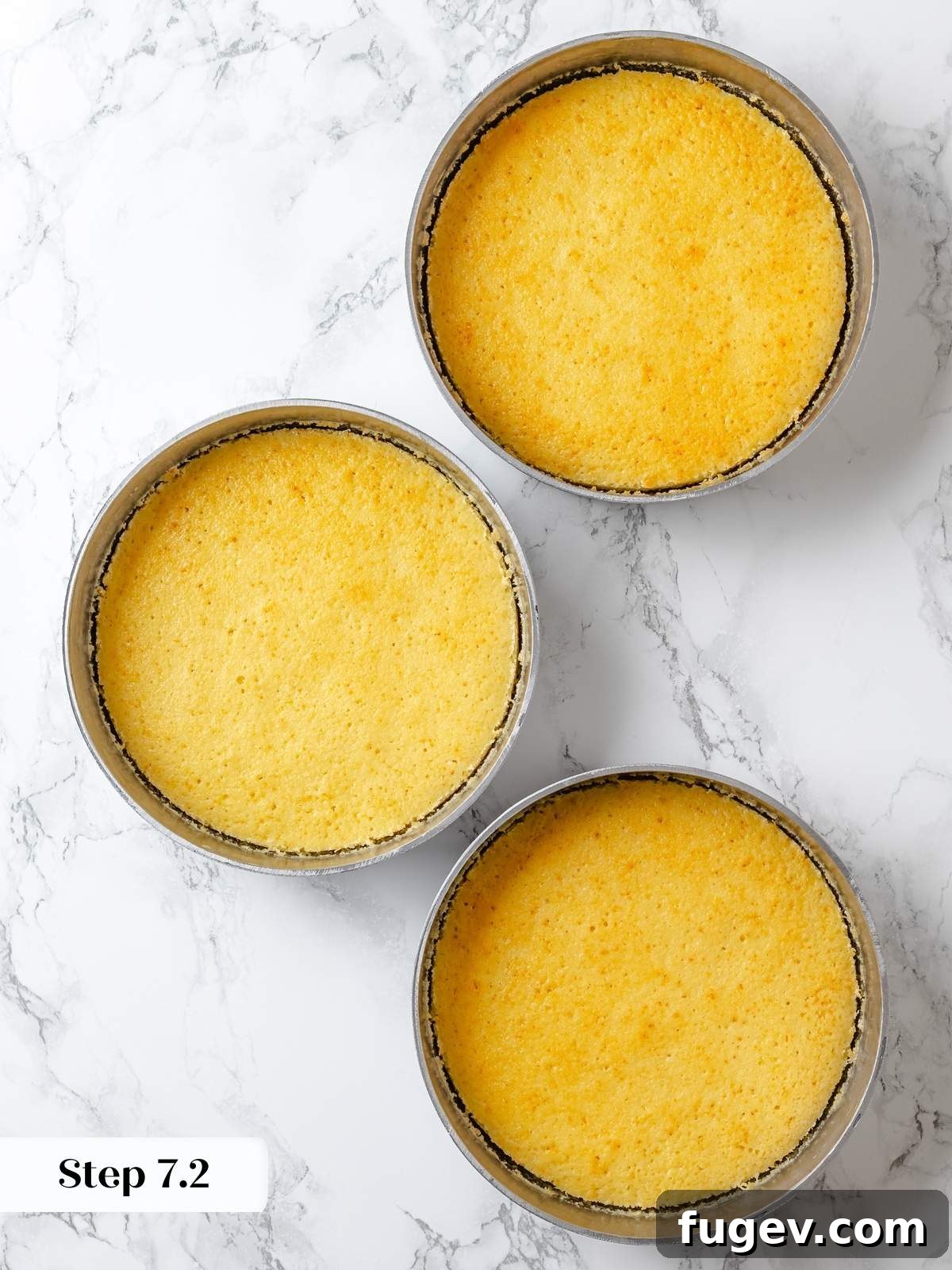 Three perfectly baked lemon cake layers, golden at the edges, cooling uniformly in their round cake pans on a wire rack.
