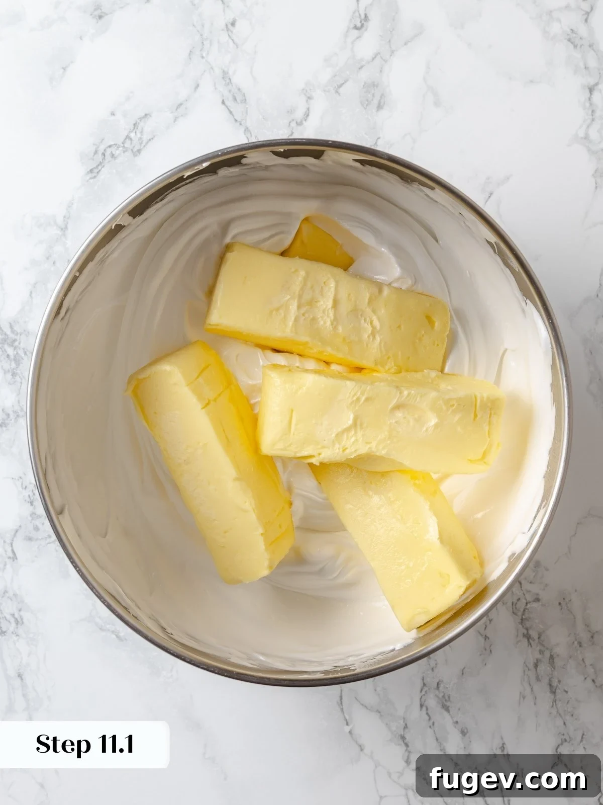 Softened butter being added gradually to the prepared meringue base during the buttercream mixing process.