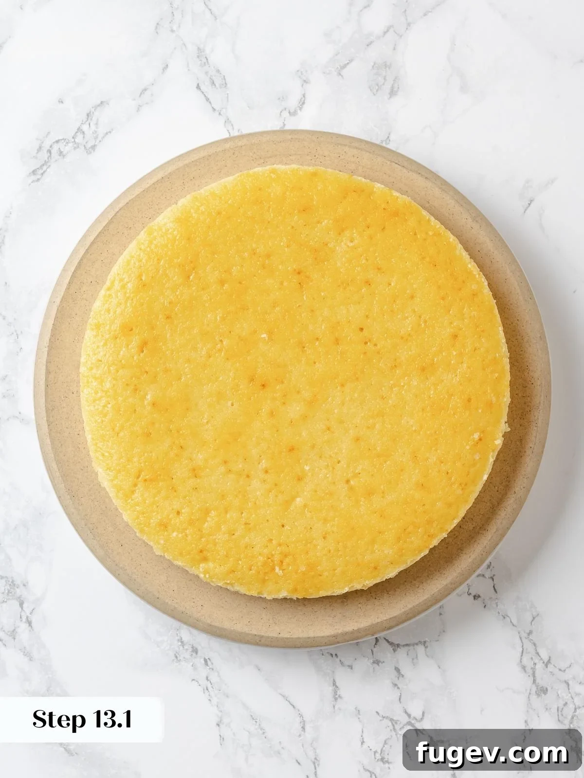 A plain, cooled lemon cake layer is carefully placed on a cake board, ready for the initial application of frosting.
