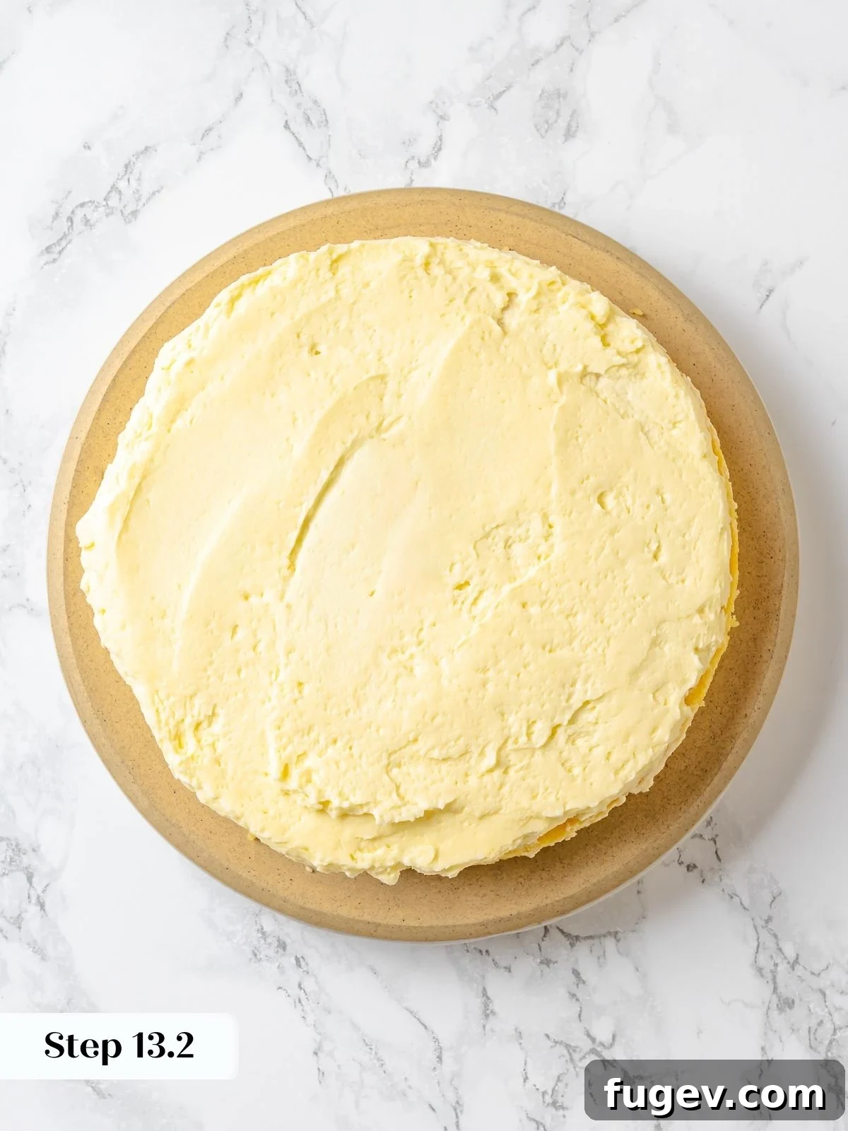 A lemon cake layer topped with a generous, smooth spread of lemon Swiss meringue buttercream, ready for the next layer.