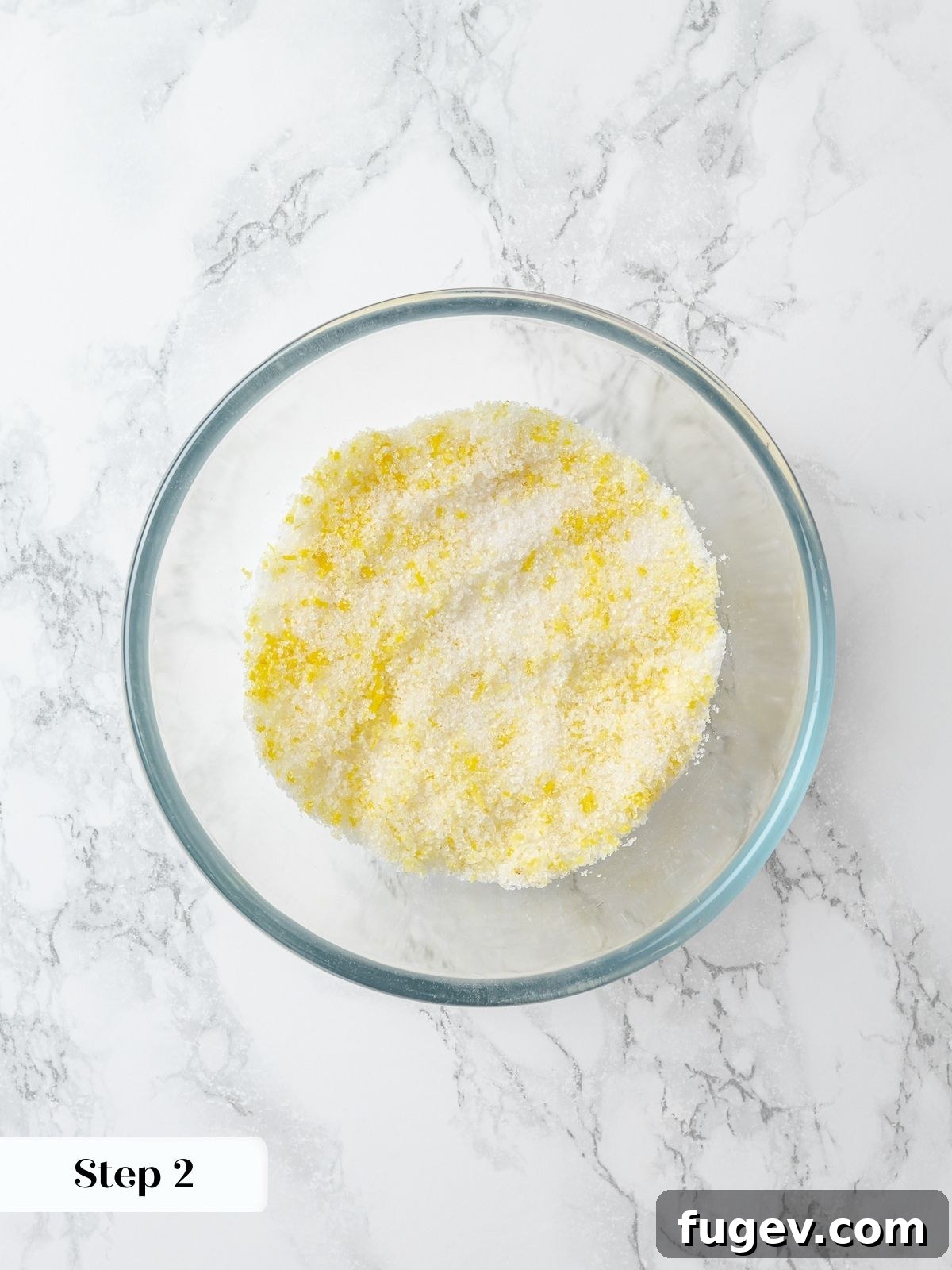 Granulated sugar being thoroughly mixed with fresh lemon zest, releasing fragrant citrus oils for maximum flavor infusion.