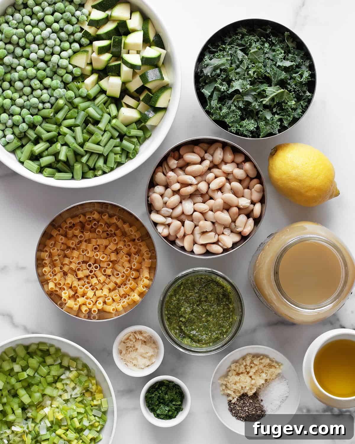Vibrant Garden Minestrone 3 A collection of fresh ingredients for green minestrone soup, including leeks, celery, green beans, zucchini, peas, kale, white beans, vegetable broth, and olive oil, laid out on a kitchen counter.