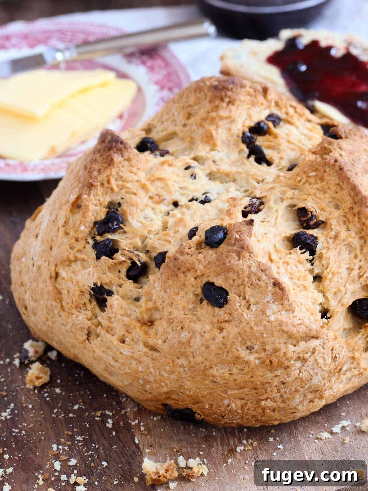 Simple Sweet Irish Raisin Bread 2 Freshly baked traditional Irish soda bread with raisins on a wooden board, surrounded by crumbs.