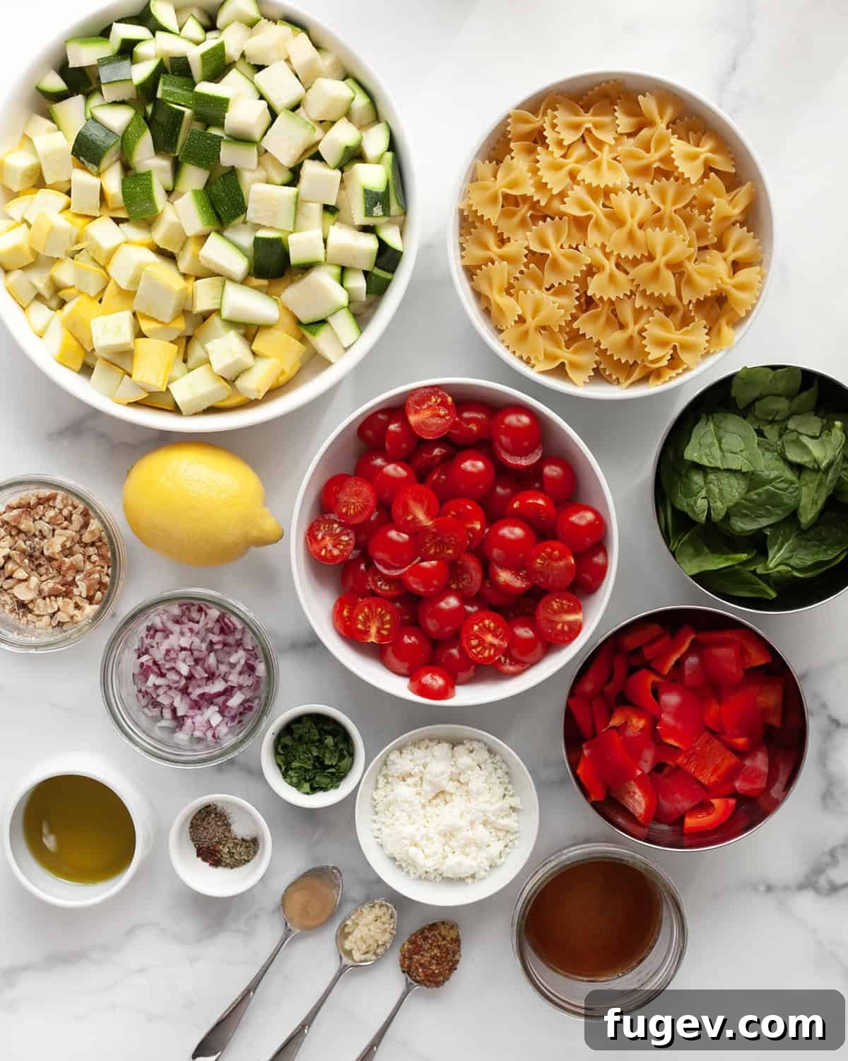 Golden Roasted Veggie Farfalle Salad 3 A selection of fresh ingredients laid out for the pasta salad, including zucchini, yellow squash, bell peppers, tomatoes, bow tie pasta, baby spinach, red onions, walnuts, lemon, seasonings, and olive oil.