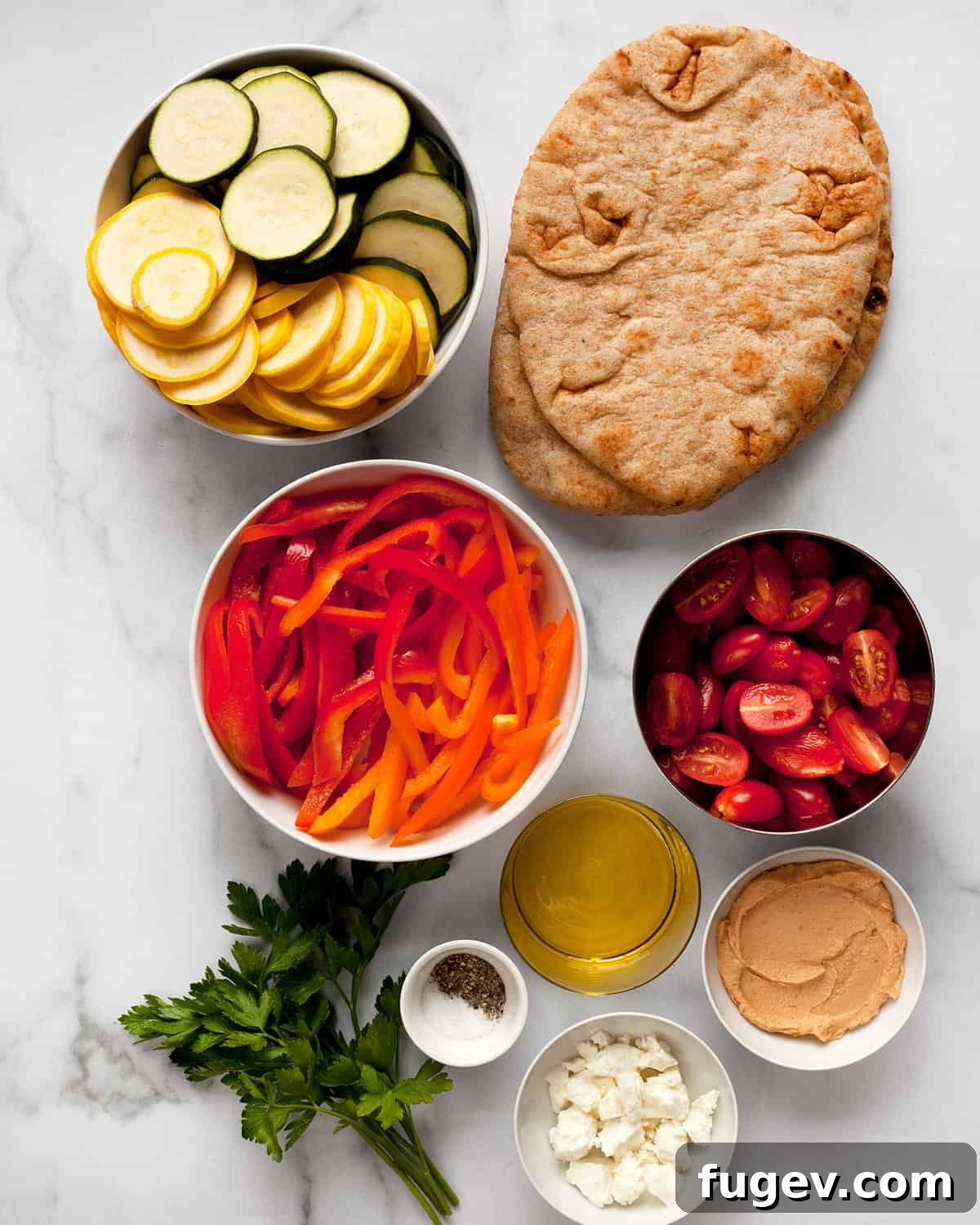 Roasted Garden Vegetable Naan Flatbread 3 A visual display of fresh ingredients including naan bread, colorful vegetables, a bowl of hummus, and a bottle of olive oil.