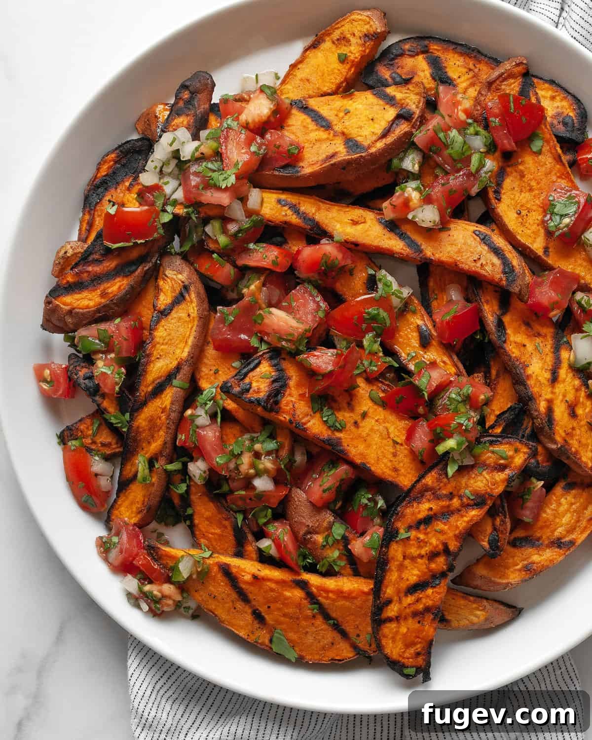 Effortlessly Delicious Grilled Sweet Potatoes 7 A close-up of a plate of grilled sweet potatoes, beautifully garnished with fresh pico de gallo and a sprig of cilantro, ready to be served.