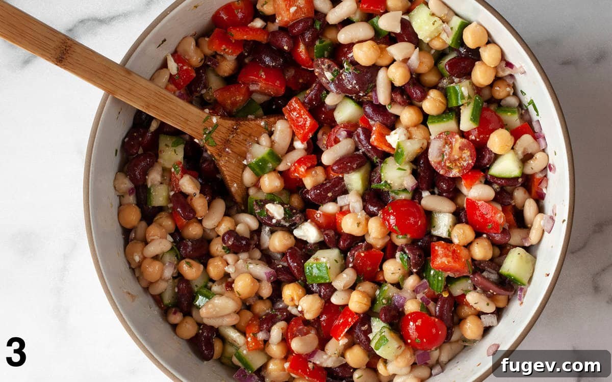 Vibrant Mediterranean Bean Medley 5 The Mediterranean bean salad, fully mixed with vinaigrette, in a large mixing bowl, ready to be served.