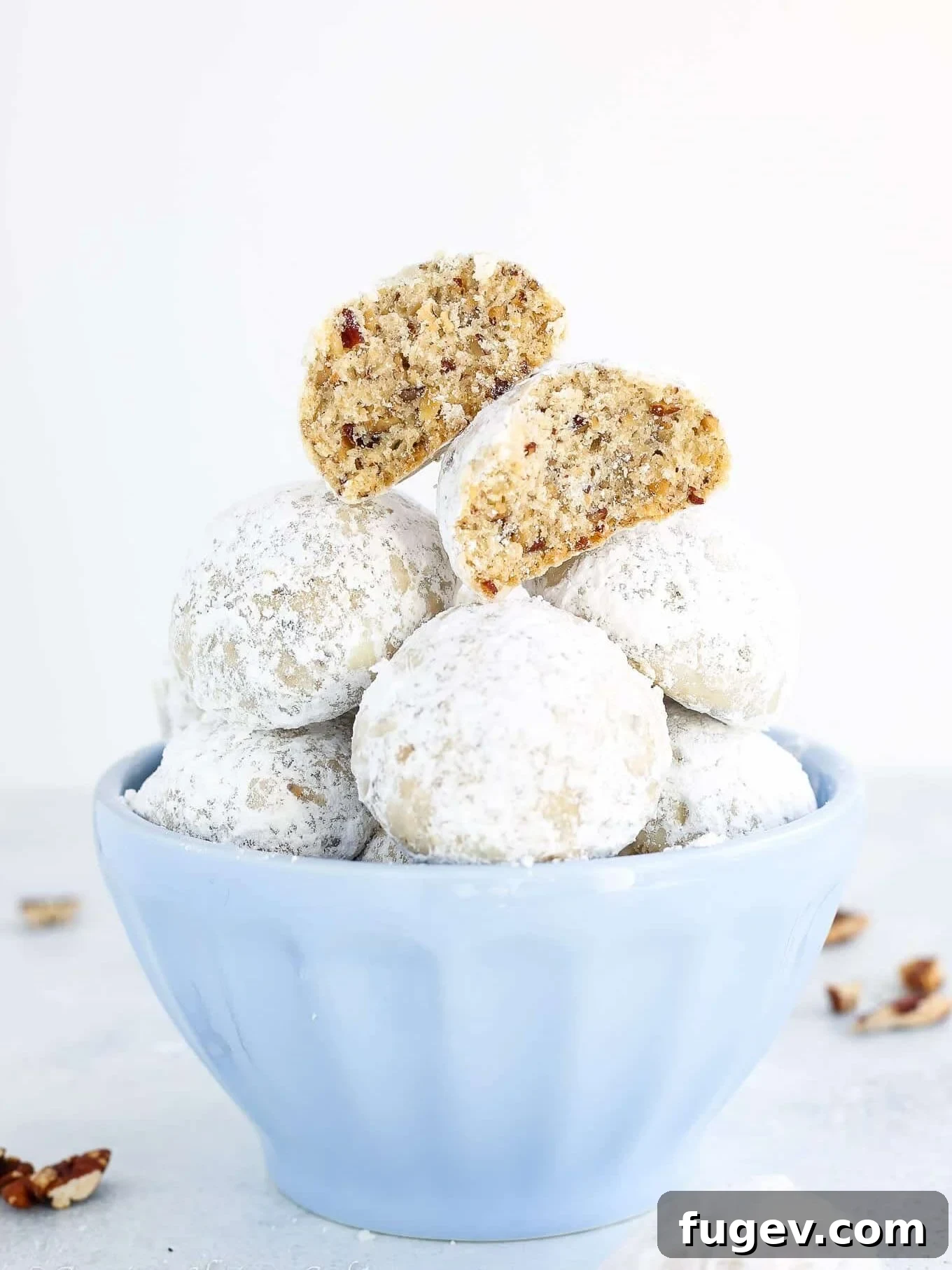 Fiesta Snowball Cookies 2 Stacked Mexican wedding cookies coated in powdered sugar in a bowl.
