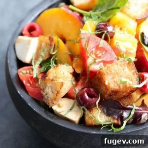 Stone Fruit Caprese Panzanella Salad in a black wooden bowl, garnished with fresh basil leaves, ready to be served.