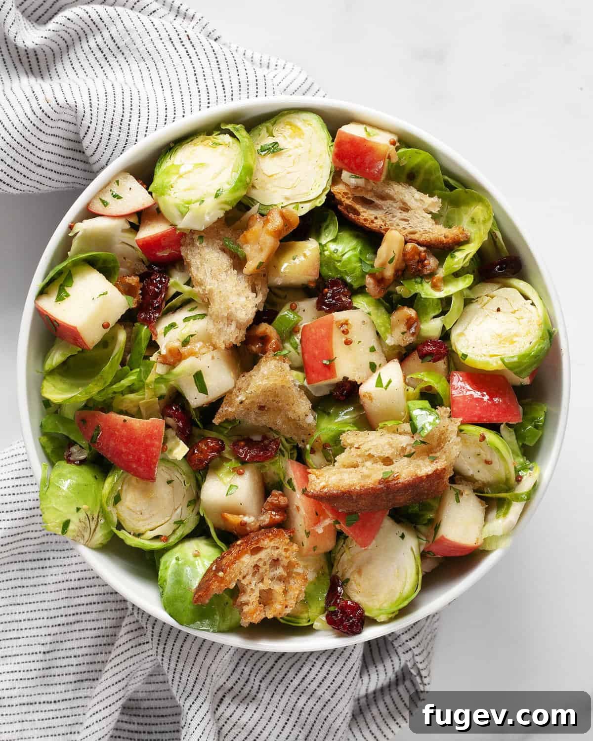 Shaved Brussels Sprout Salad with Crisp Apples and Toasted Walnuts 7 A beautifully presented bowl of Brussels sprout apple salad, featuring thinly sliced sprouts, diced apples, toasted walnuts, and dried cranberries, all glistening with vinaigrette, ready to be enjoyed.