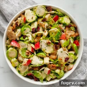 Shaved Brussels Sprout Salad with Crisp Apples and Toasted Walnuts 8 Brussels sprout salad with apples, walnuts, dried cranberries and croutons in a bowl.