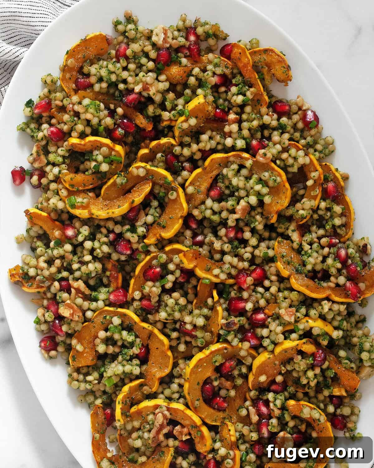 Caramelized Delicata Squash Couscous 2 Roasted delicata squash couscous on a serving platter, garnished with fresh herbs and pomegranate seeds.