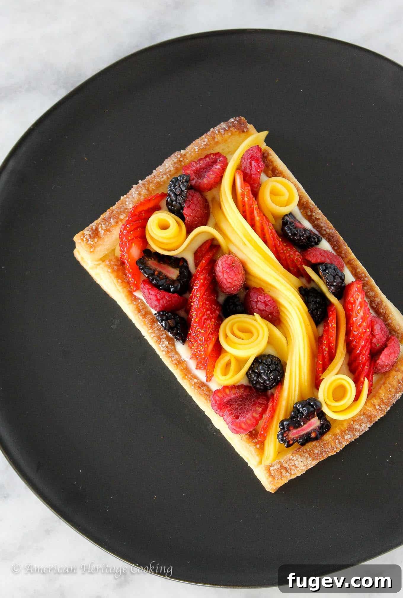 Flaky Fruit Delight 2 A beautifully arranged puff pastry fruit tart on a black plate, resting on a white marble surface, showcasing vibrant fresh fruits and flaky crust.