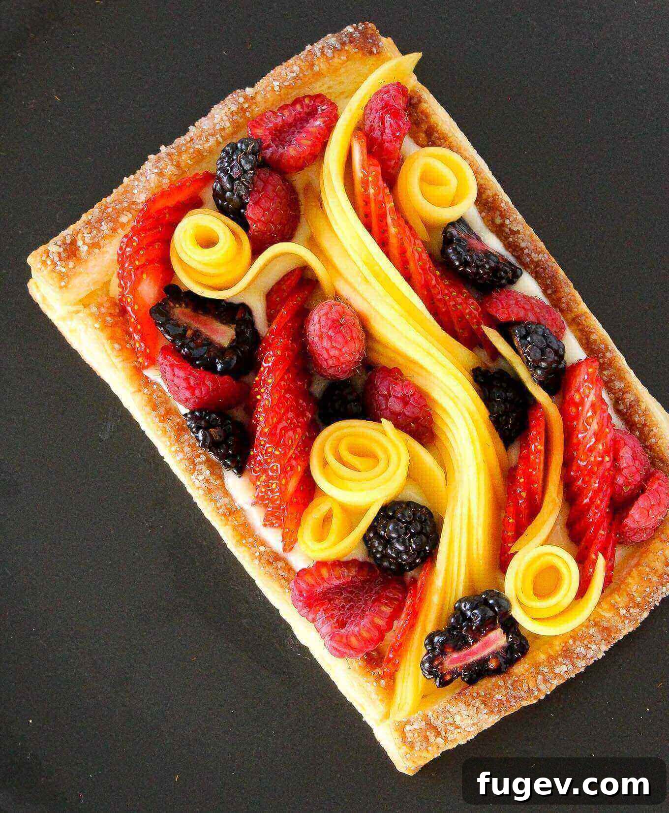 Flaky Fruit Delight 4 An elegantly styled puff pastry tart featuring a central line of sliced mango surrounded by fresh raspberries and blackberries.