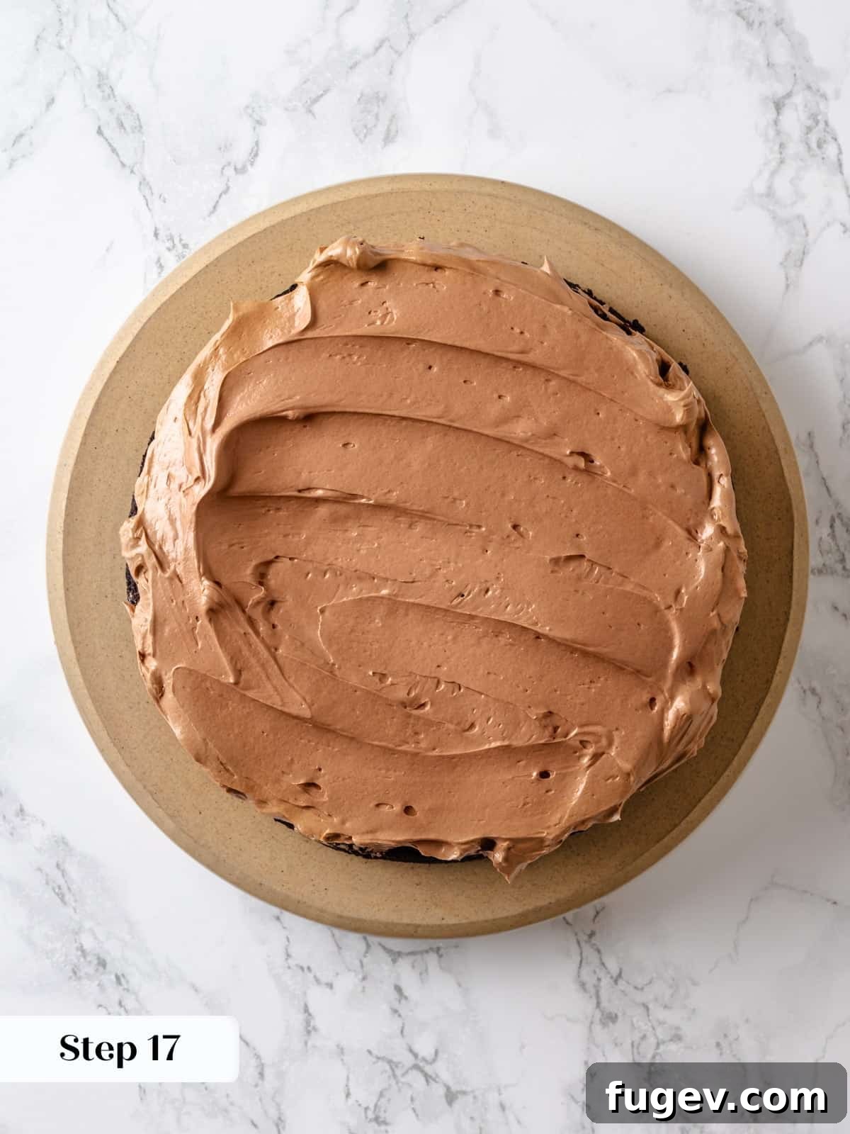 Sinfully Rich Chocolate Delight 23 Chocolate Swiss meringue buttercream being evenly spread across a cake layer using a large offset spatula, preparing for the next layer.