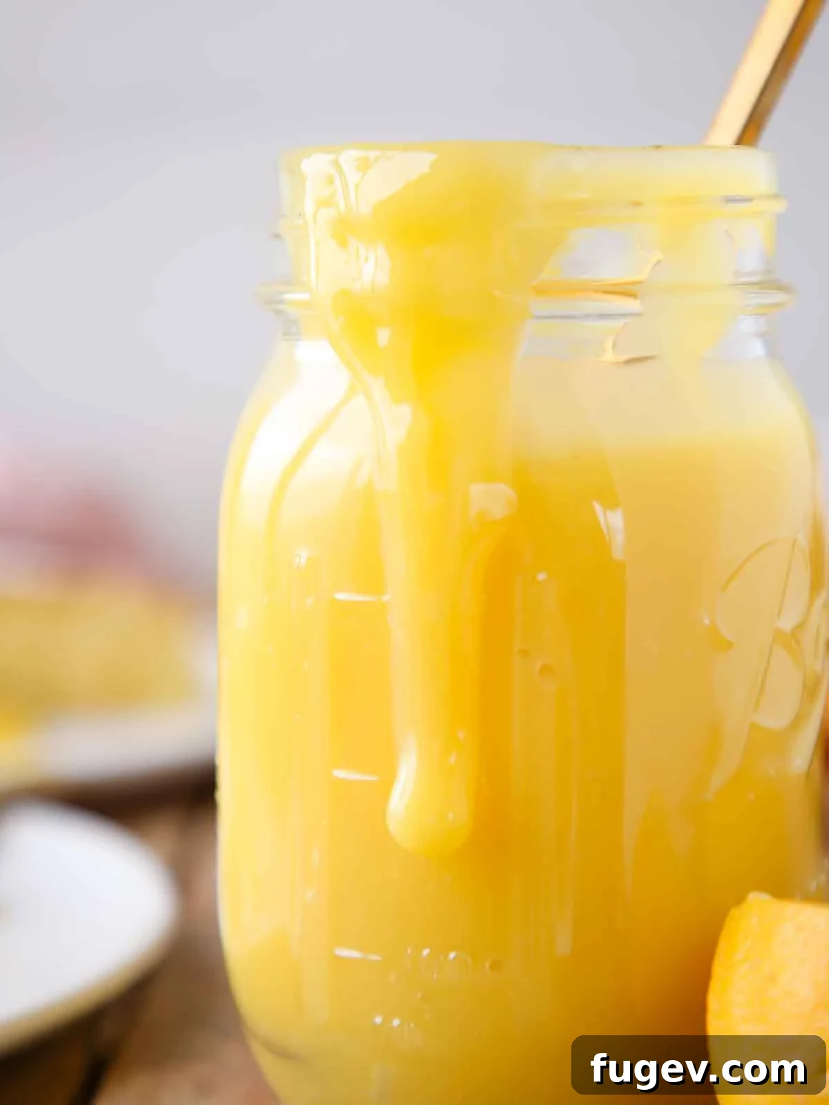 Bright & Tangy Lemon Curd 2 A mason jar overflowing with vibrant yellow lemon curd, with a slice of cake subtly blurred in the background, hinting at delicious dessert pairings.