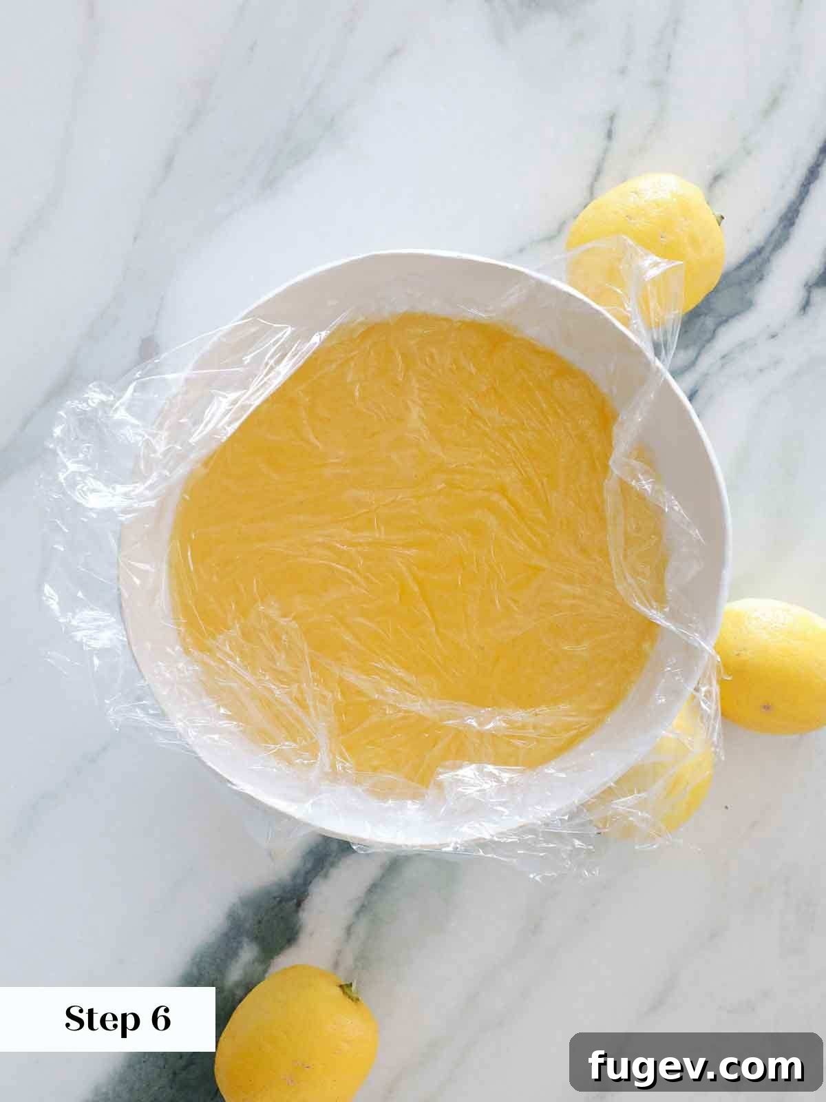 Bright & Tangy Lemon Curd 11 Hot lemon curd cooling in a white bowl, covered tightly with plastic wrap directly on its surface to prevent a skin from forming.