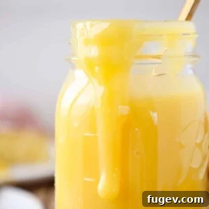 Close-up of golden lemon curd delicately dripping down the side of a clear mason jar, showcasing its smooth texture.