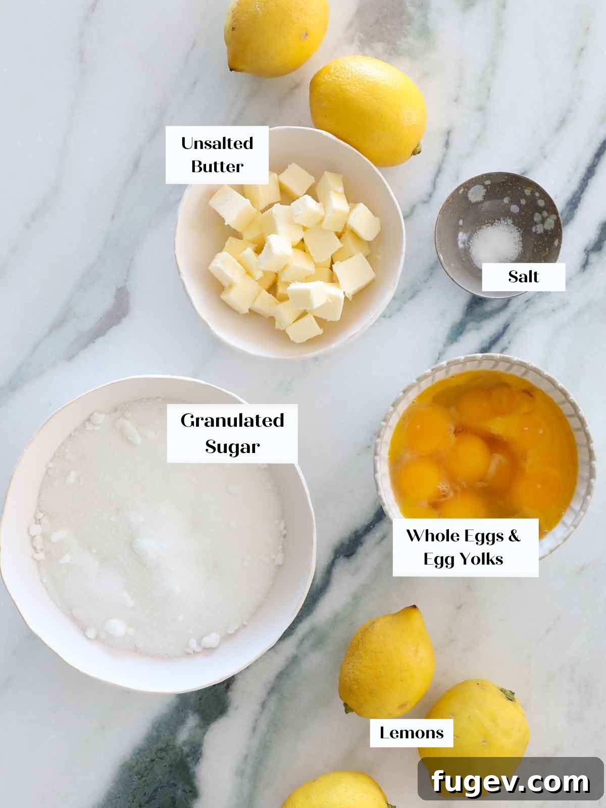 Bright & Tangy Lemon Curd 4 All the fresh ingredients for homemade lemon curd neatly arranged on a pristine marble surface, including bright yellow lemons, eggs, sugar, and a stick of butter.