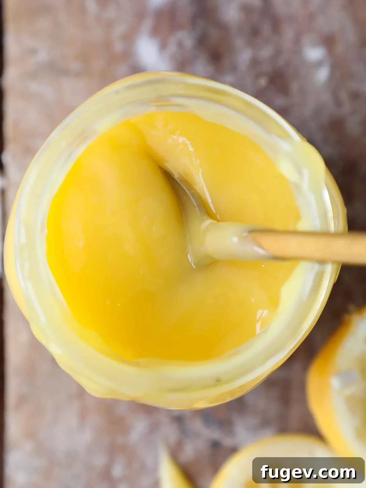 Bright & Tangy Lemon Curd 5 A close-up shot of the top of a mason jar filled with bright lemon curd, with a small silver spoon resting on the rim, inviting a taste.