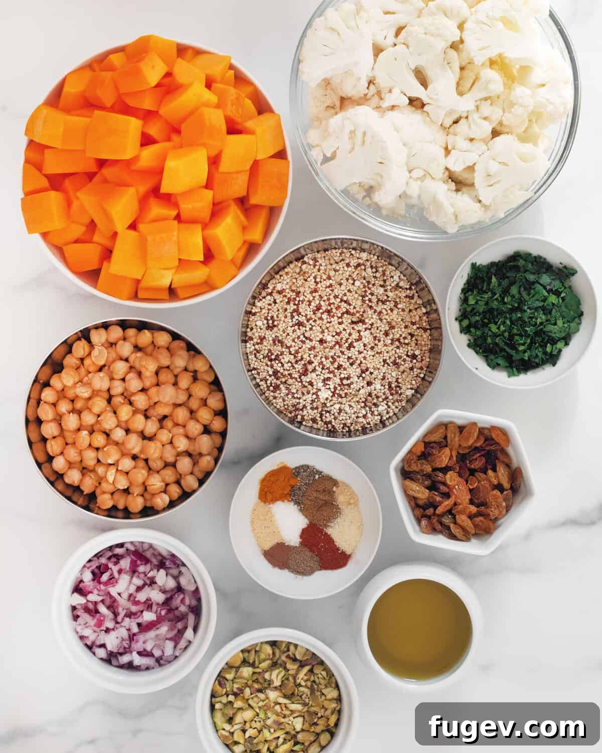 Hearty Roasted Butternut Squash and Cauliflower Quinoa 3 A vibrant flat lay showcasing all the fresh and dried ingredients: butternut squash, cauliflower, uncooked quinoa, canned chickpeas, red onions, fresh parsley, golden raisins, shelled pistachios, olive oil, and a selection of dried spices.