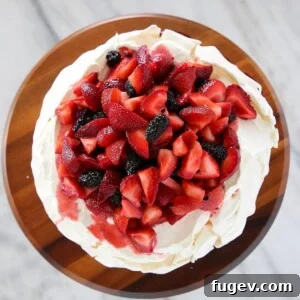 The best pavlova dessert, generously topped with tangy lemon curd, an assortment of fresh mixed fruit, and a dusting of powdered sugar.