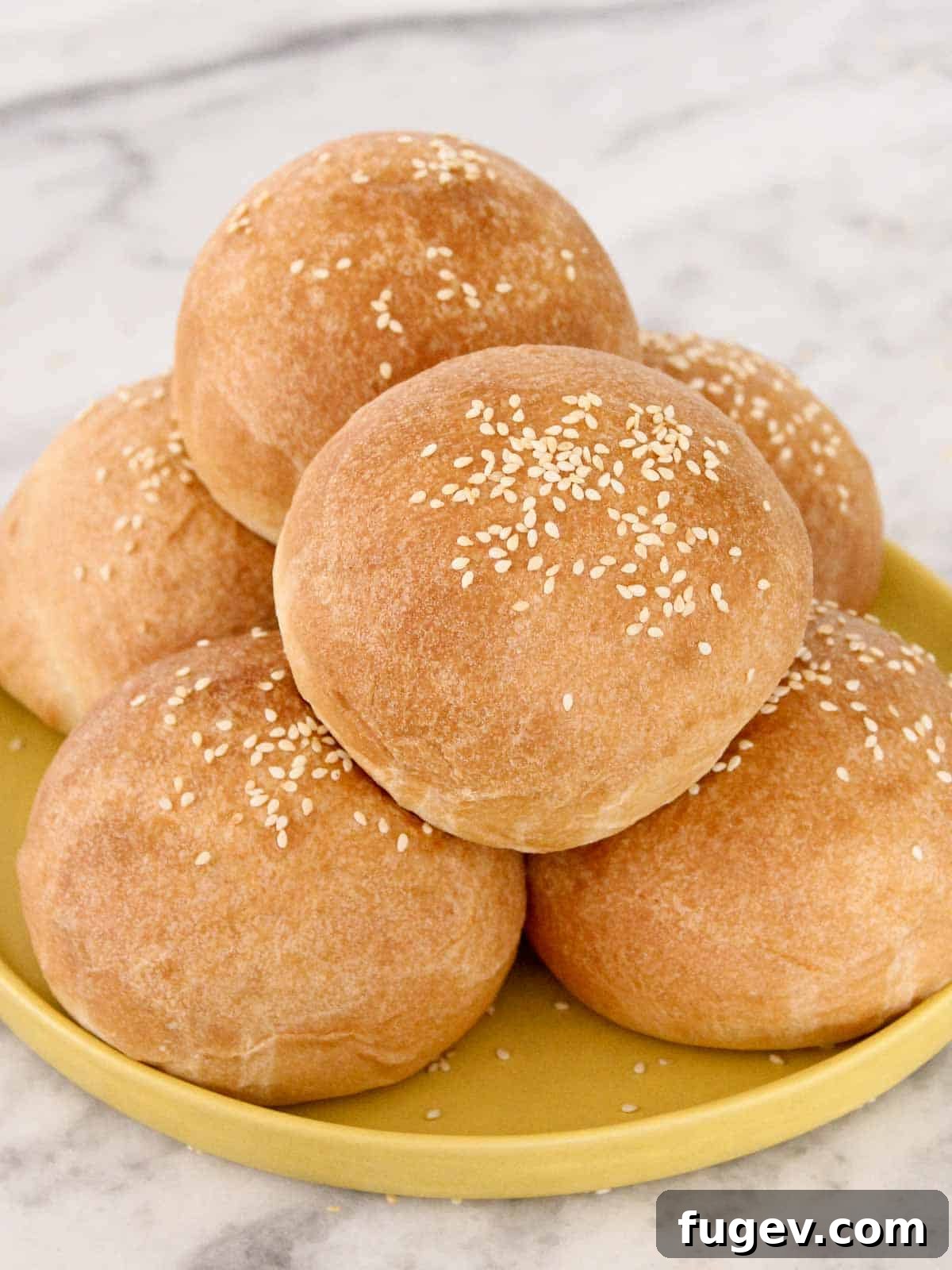 Perfect Fluffy Brioche Buns 2 Freshly baked brioche hamburger buns with sesame seeds on a vibrant yellow plate, highlighting their golden-brown crust and fluffy texture.