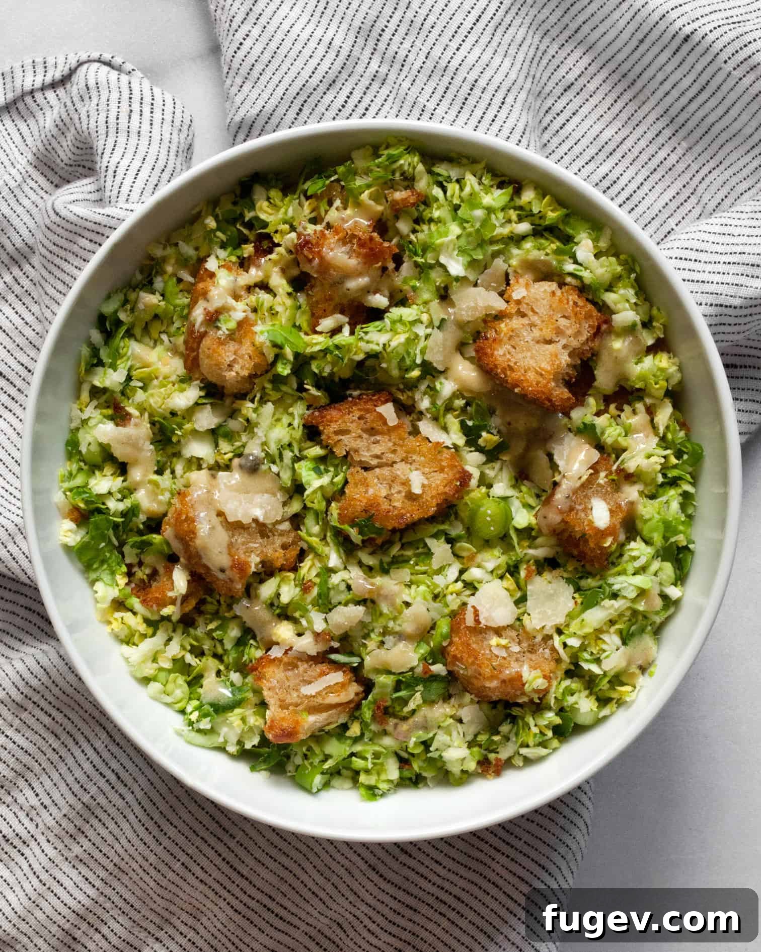 Shaved Brussels Sprout Caesar Salad 6 A generous serving of shredded brussels sprout Caesar salad, perfectly tossed and ready to be enjoyed, presented in an elegant ceramic bowl.