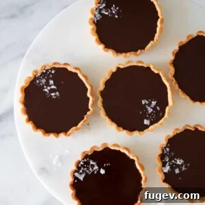 Silky Chocolate Delights 2 Mini salted chocolate tarts arranged on a marble cake stand, garnished with flaky sea salt.
