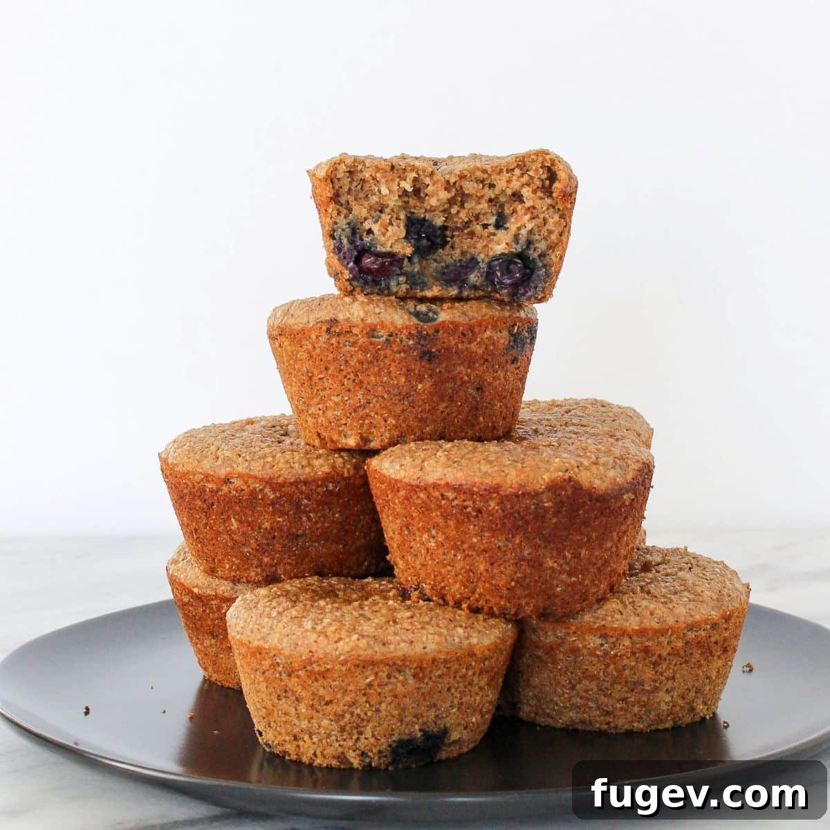Power-Packed Banana Muffins 4 A banana protein muffin with one bite taken, stacked with others, showcasing its soft and moist internal texture and visible blueberries.