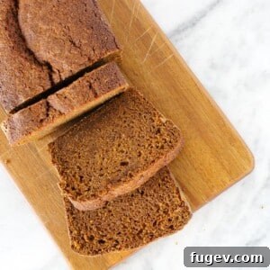 Sliced pumpkin bread on a wooden board against a marble counter, enticingly presented.