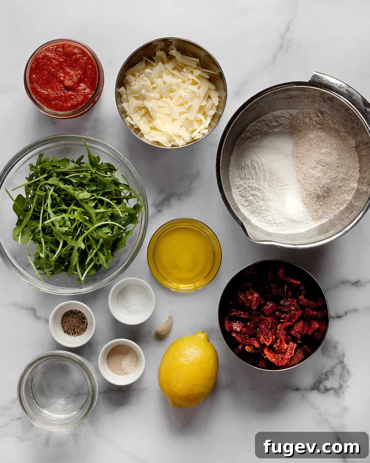 Charred Arugula and Sun-Kissed Tomato Pizza 3 Various ingredients for the pizza including fresh arugula, sun-dried tomatoes, tomato sauce, garlic, and cheese.